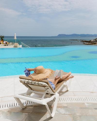 a woman laying on a lounge chair next to a swimming pool at Leptos Panorama Hotel in Kalamaki Chanion