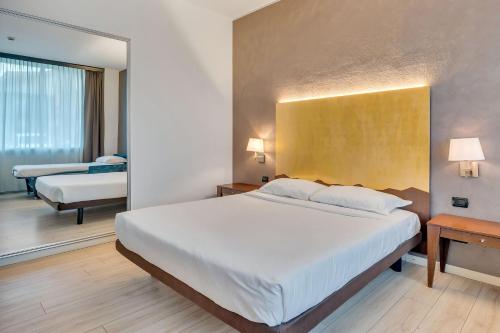 a bedroom with a large white bed and two tables at B&B HOTEL Bergamo Executive in San Paolo D'Argon