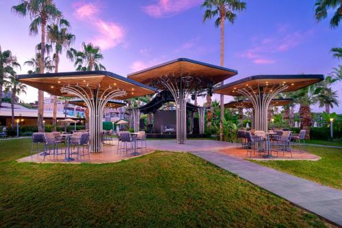 a patio with tables and chairs in a park with palm trees at Leodikya Kirman Premium - Ultra All Inclusive in Okurcalar