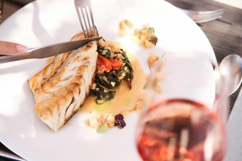 a white plate with a piece of fish and a glass of wine at NEMA Design Hotel & Spa - Adults Only in Hersonissos