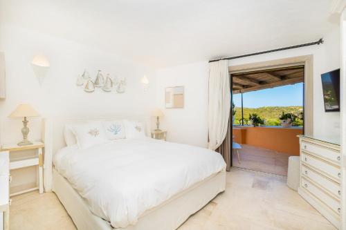 a bedroom with a white bed and a sliding glass door at Luxury Pevero Apartment in Golf Club in Abbiadori