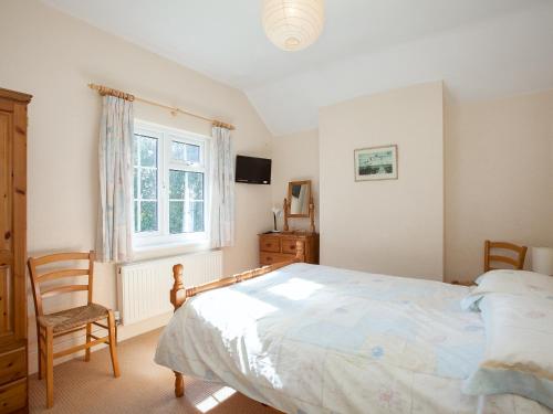 a bedroom with a bed and a chair and a window at Fir Tree Cottage in Standon