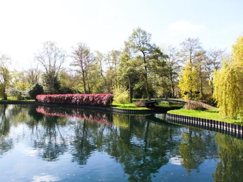 a river in a park with a bridge and pink flowers at Swallowtail Lodge in Brundall