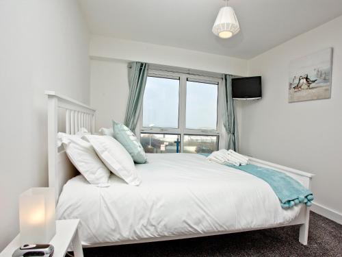 a white bedroom with a bed with a window at Fistral Escape in Crantock