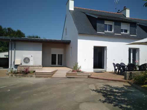 Cette maison blanche dispose d'une terrasse avec des chaises et des tables. dans l'établissement Maison bord de mer - Baie de Douarnenez - Piscine couverte, à PloÃ©ven