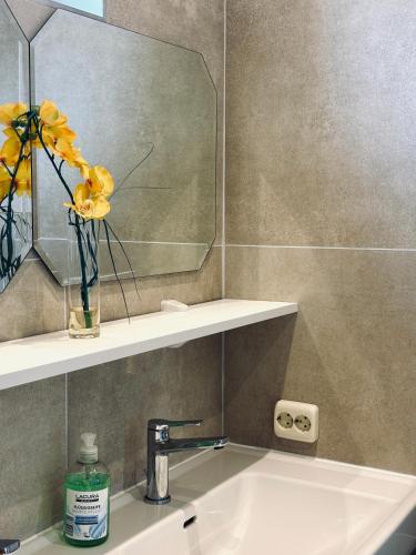 a bathroom sink with a mirror and a vase with yellow flowers at Sunlit Apartment with Garden, Next to Station, Vienna in Vösendorf