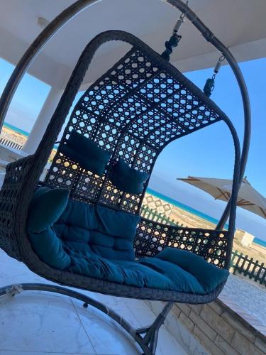 a wicker chair with blue pillows on a balcony at First Row Sea-Front Chalets Media Village in Marsa Matruh