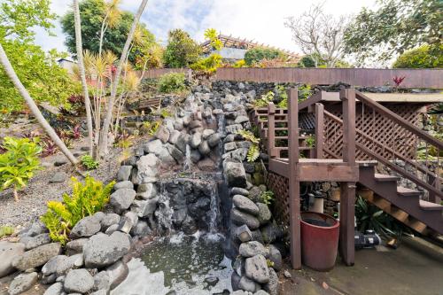 a waterfall in a garden with a wooden bridge at Aloha Casa Miramar by SkyRun Kona Coast in Kailua-Kona