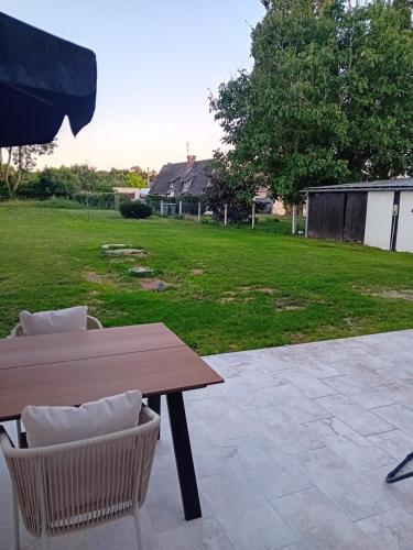 a wooden table and chairs on a patio with a yard at Le gîte de notre histoire in Épégard