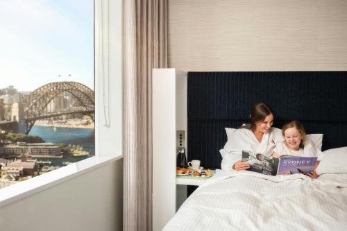 a woman and a child laying in bed with a book at Sydney Harbour Marriott Hotel at Circular Quay in Sydney