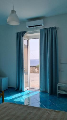 a room with a sliding glass door with blue curtains at Brezza di Terra in Santa Marina Salina