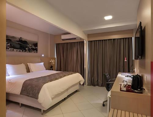 une chambre avec un lit, un bureau et une télévision dans l'établissement Rio Plaza - Suítes no Rio de Janeiro por Carpediem, à Rio de Janeiro