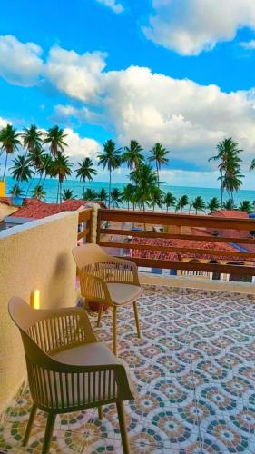 a patio with two benches and palm trees and the ocean at Japaratinga Suites in Japaratinga