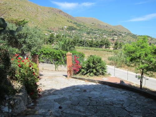 a driveway with flowers and a mountain in the background at Palms Villa in Scopello
