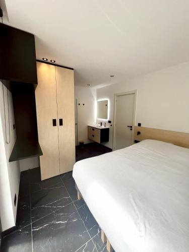 a bedroom with a large white bed and a kitchen at Serenity Lodge Durbuy - Sauna & Jacuzzi in Durbuy