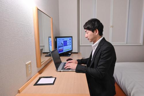 a man in a suit sitting at a desk with a laptop at Sanco Inn Kuwana Ekimae in Kuwana