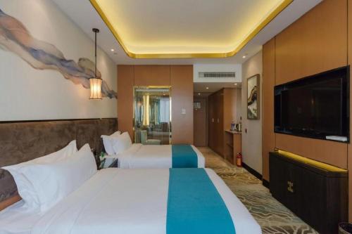 a hotel room with two beds and a flat screen tv at Bati Holiday Hotel in Zhongshan