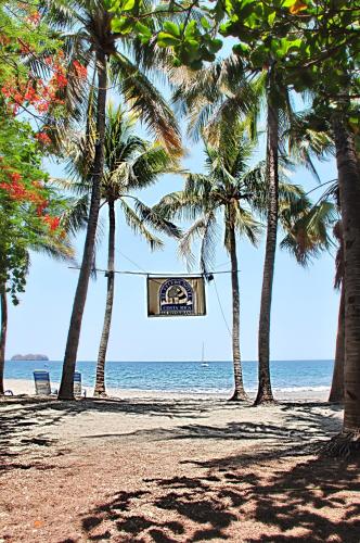a sign on a beach with palm trees and the ocean at Hotel El Velero in Playa Hermosa