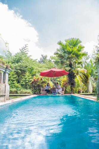 two people sitting under an umbrella next to a swimming pool at Avalon Ubud Castle & SPA in Ubud