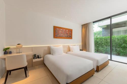 a hotel room with two beds and a desk and a window at Naman Retreat in Da Nang