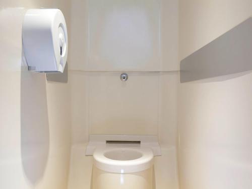a white bathroom with a toilet with a paper dispenser at UNISOTEL ex hotelF1 Saint Brieuc in Tregueux