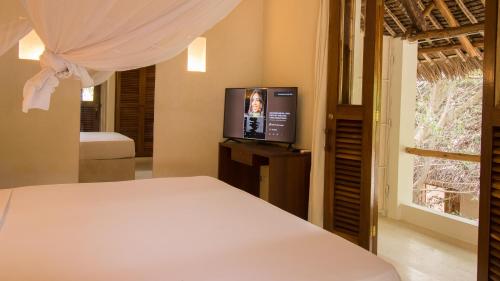 a bedroom with a bed and a flat screen tv at Palm Garden ECO Boutique Hotel No Kids under 12 in Watamu