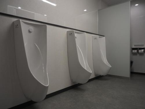 a row of white urinals in a public bathroom at Capsule Hostel Beppu Tower in Beppu