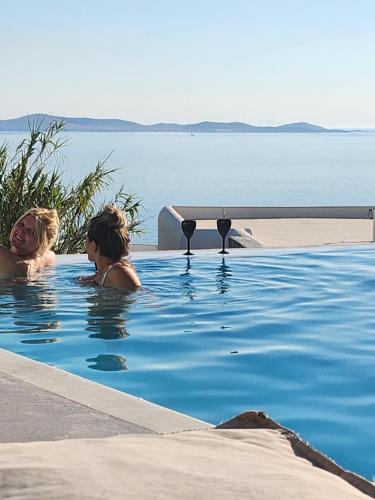 two women in a swimming pool next to the water at ELLI TROPiCAL LUXURY SUITES SUNSET-INFINITY POOL- SEA SIDE-NEAR CENTER PARKING in Mikonos