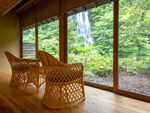 two wicker chairs sitting on a porch with a waterfall out the window at Yumoto Kissho in Osaki