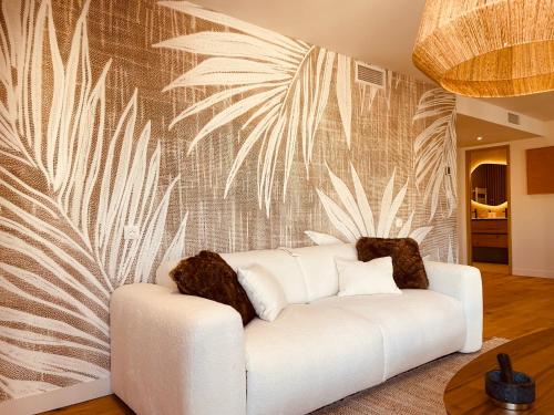 a white couch in a living room with a palm wallpaper at La Maison Cavet 5 Appartements de standing au cœur du village in Sanary-sur-Mer