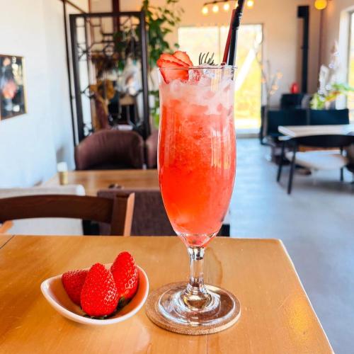 a drink sitting on a table next to a bowl of strawberries at Guesthouse ＆ Beach Cafe Fuego in Hyuga