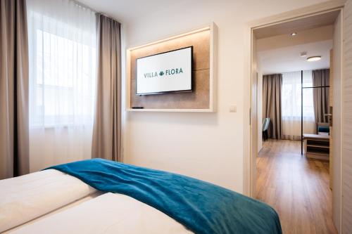 a bedroom with a bed and a television on a wall at Hotel Villa Flora in Velden am Wörthersee