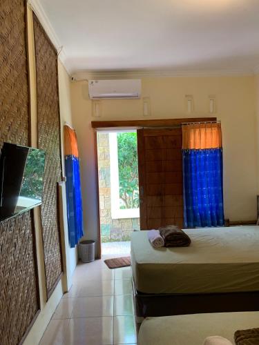 a bedroom with two beds and a window with blue curtains at Pondok Elen Mandalika in Praya