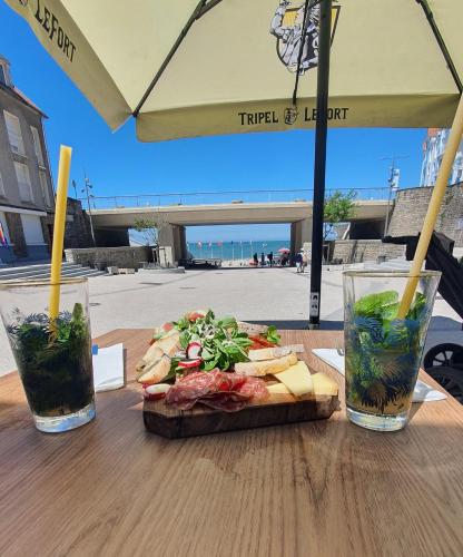 a sandwich and two drinks on a wooden table at l'echo des vagues ,face mer, vue imprenable, appartement pour 2 à 4 personnes in Le Portel