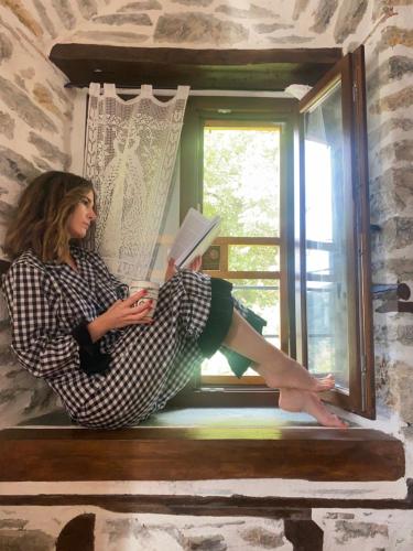 a woman sitting on a window sill reading a book at Archontiko Michael since 1868 in Vizitsa