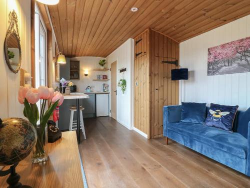a living room with a blue couch and a kitchen at Luxury Shepherd Hut with Private Hot Tub in Swaffham Bulbeck