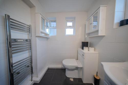 a white bathroom with a toilet and a sink at The Hampden House - Sleeps 7 in Grays Thurrock