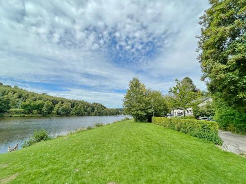 a grassy field next to a river with a house at Lakeview Vielsalm in Vielsalm