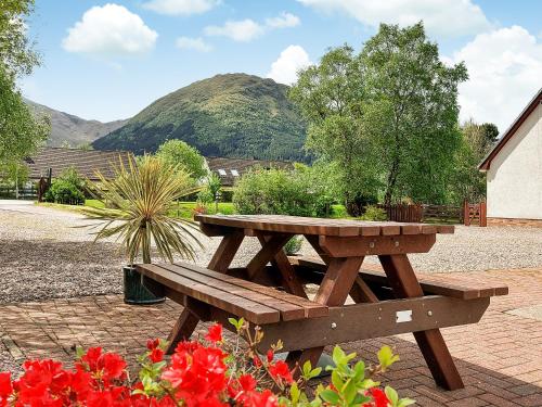 einen hölzernen Picknicktisch in einem Garten mit Blumen in der Unterkunft Roe Deer Cottage in North Ballachulish