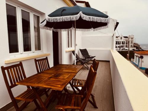 un tavolo in legno e sedie su un balcone con ombrellone di Baleal Bali Casa da Ilha a Baleal