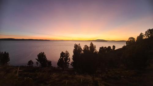 a sunset over the water with trees in the foreground at LA MANSION DEL SOL LODGE Taquile island in Isla Taquili
