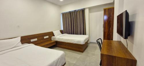 a room with two beds and a desk and a television at Hotel Maharaja Inn in Pune