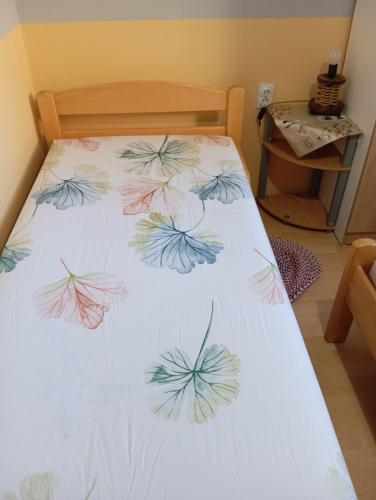 a bed with a white sheet with leaves on it at Milica Apartmani in Vrdnik