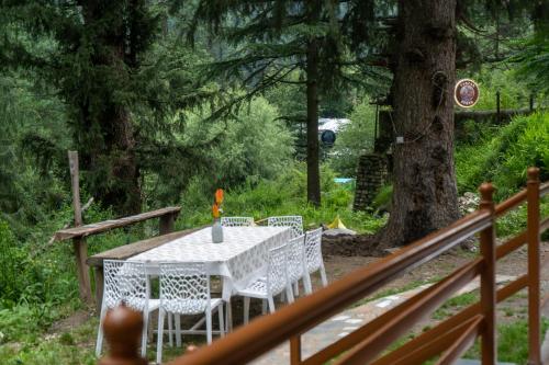 a white table and chairs on a deck with a tree at Tarzan Stays Jibhi in Shoja