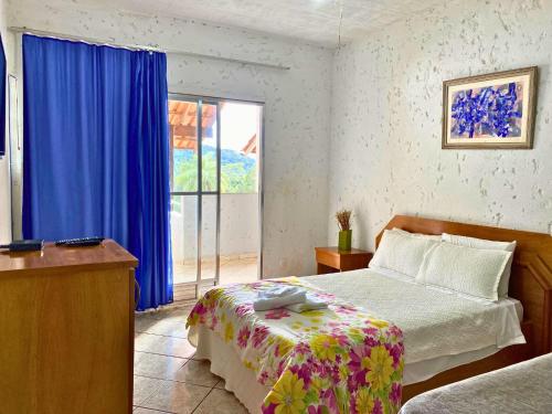 a bedroom with a bed and a window with blue curtains at Pousada Encantos da Serra Macacos in Macacos