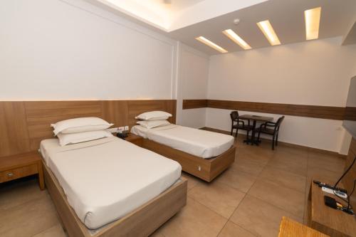 two beds in a room with a table and chairs at Hotel Luciya Palace in Trichūr