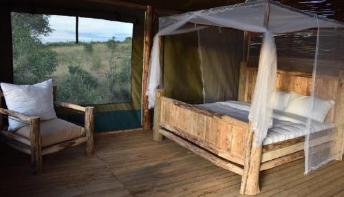 a bedroom with a canopy bed and a chair at Leopard Rest Camp in Mbarara