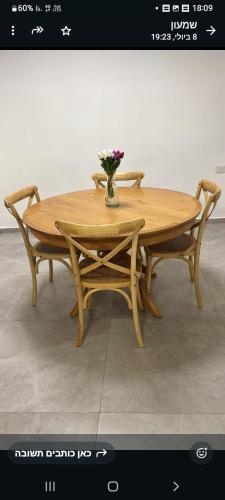 a wooden table with two chairs and a vase with flowers at הבית של רביבו in Sderot
