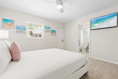 a white bedroom with a bed and a tv on the wall at Bianco Sands By Beachside Management in Siesta Key