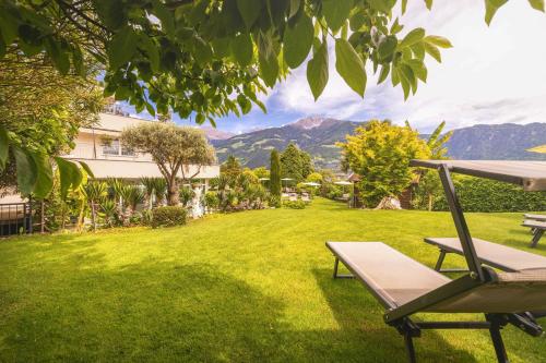 a yard with a bench and a house and mountains at Hotel Garni Herz in Tirolo